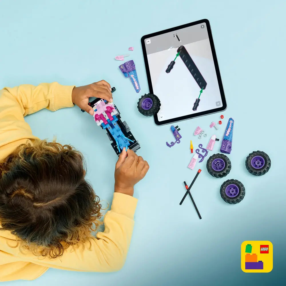 LEGO Technic Monster Jam Sparkle Smash build scene shows pink and purple Technic parts, wheels, and axles arranged on a light blue surface as a child assembles the pull-back monster truck using tablet instructions.