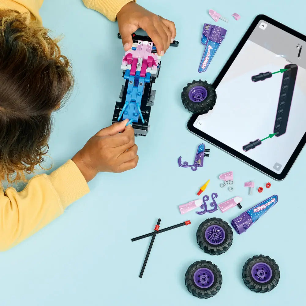 LEGO Technic Monster Jam Sparkle Smash build activity shows a child attaching colorful Technic beams, axles, and decorative panels to the chassis while following step-by-step digital building instructions.