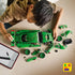 LEGO Technic Porsche 911 GT3 R building scene shows green plastic Technic chassis and loose components spread on a table as a child assembles the race car using a digital instruction app in a bright indoor setting.
