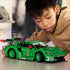 LEGO Technic Porsche 911 GT3 R lifestyle image shows a child focused on assembling the green race car model, holding detailed Technic components and aligning parts on a tabletop in a warm indoor environment.
