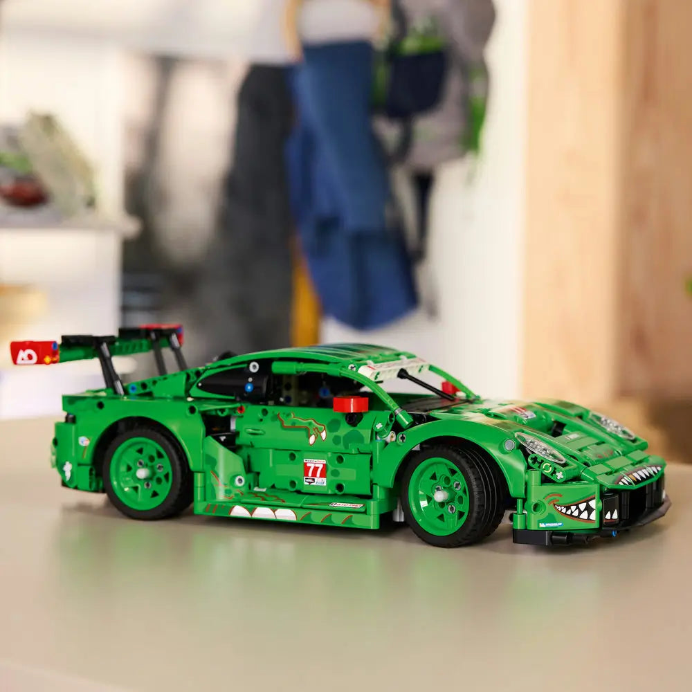 LEGO Technic Porsche 911 GT3 R model displayed fully built with green bodywork, racing decals, large rear wing, low aerodynamic stance, and rolling wheels positioned on a smooth table in a home setting.