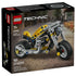 LEGO Technic yellow motorcycle set features a bright yellow and gray plastic bike with black frame, rubber tires, and visible mechanical parts, designed as a compact motorbike model, shown on branded packaging with an urban street background.