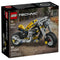 LEGO Technic yellow motorcycle set features a bright yellow and gray plastic bike with black frame, rubber tires, and visible mechanical parts, designed as a compact motorbike model, shown on branded packaging with an urban street background.