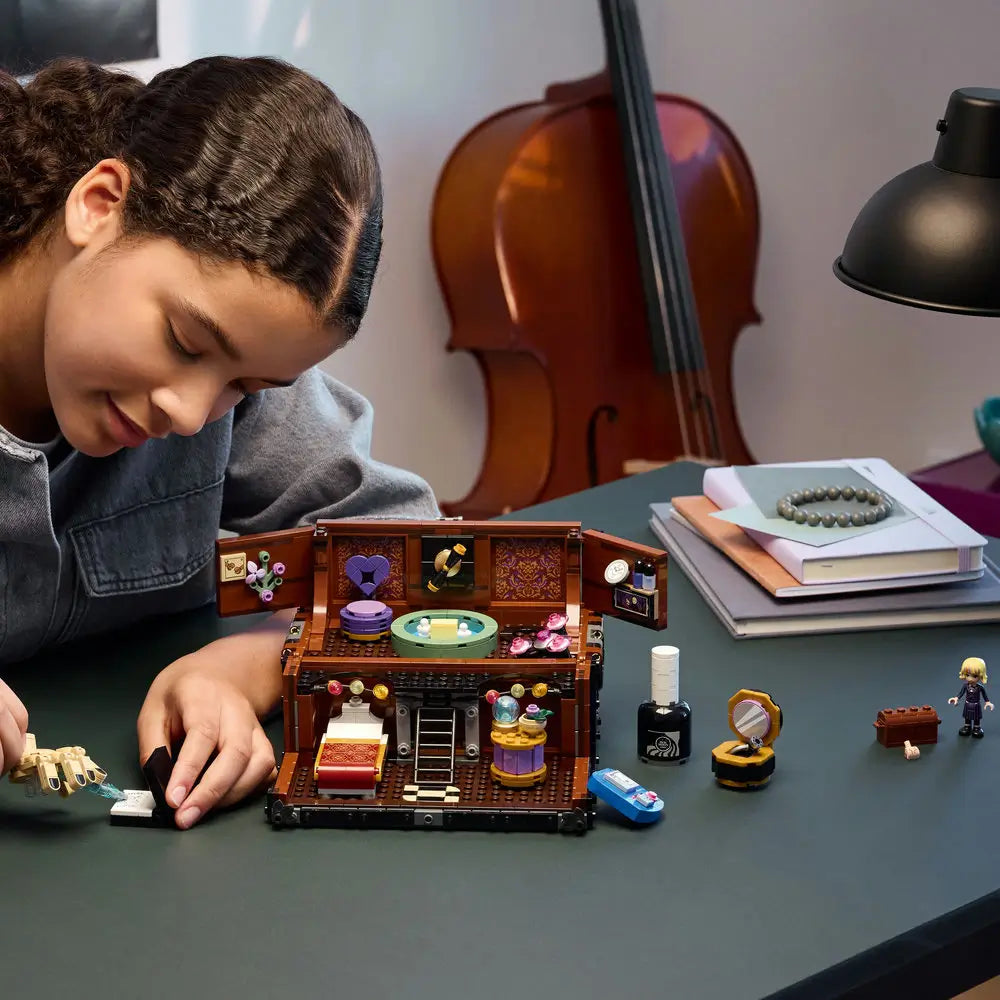 Child building LEGO Wednesday Thing’s Apartment set, showing a detailed miniature room with bed, potion bottles, and the iconic Thing hand figure on a desk under soft lighting.