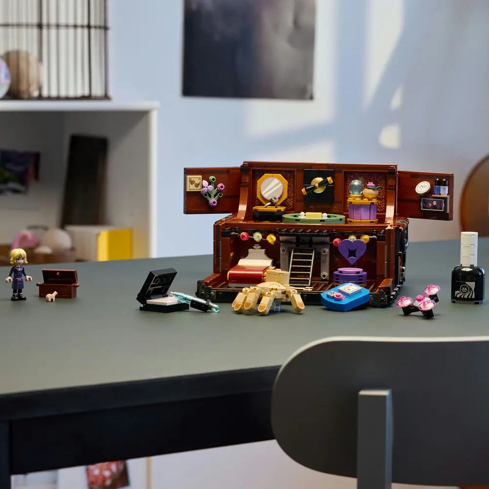 LEGO Wednesday Thing’s Apartment model displayed on a desk with included accessories like perfume bottles, a typewriter, a chest, and a small purple heart detail, illuminated by natural light.