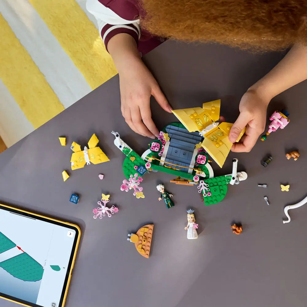 LEGO Wicked Glinda's Wedding Day playset shows a child building the colorful wedding scene with butterfly models, mini-dolls and accessories on an indoor table with detailed LEGO elements and realistic display presentation.