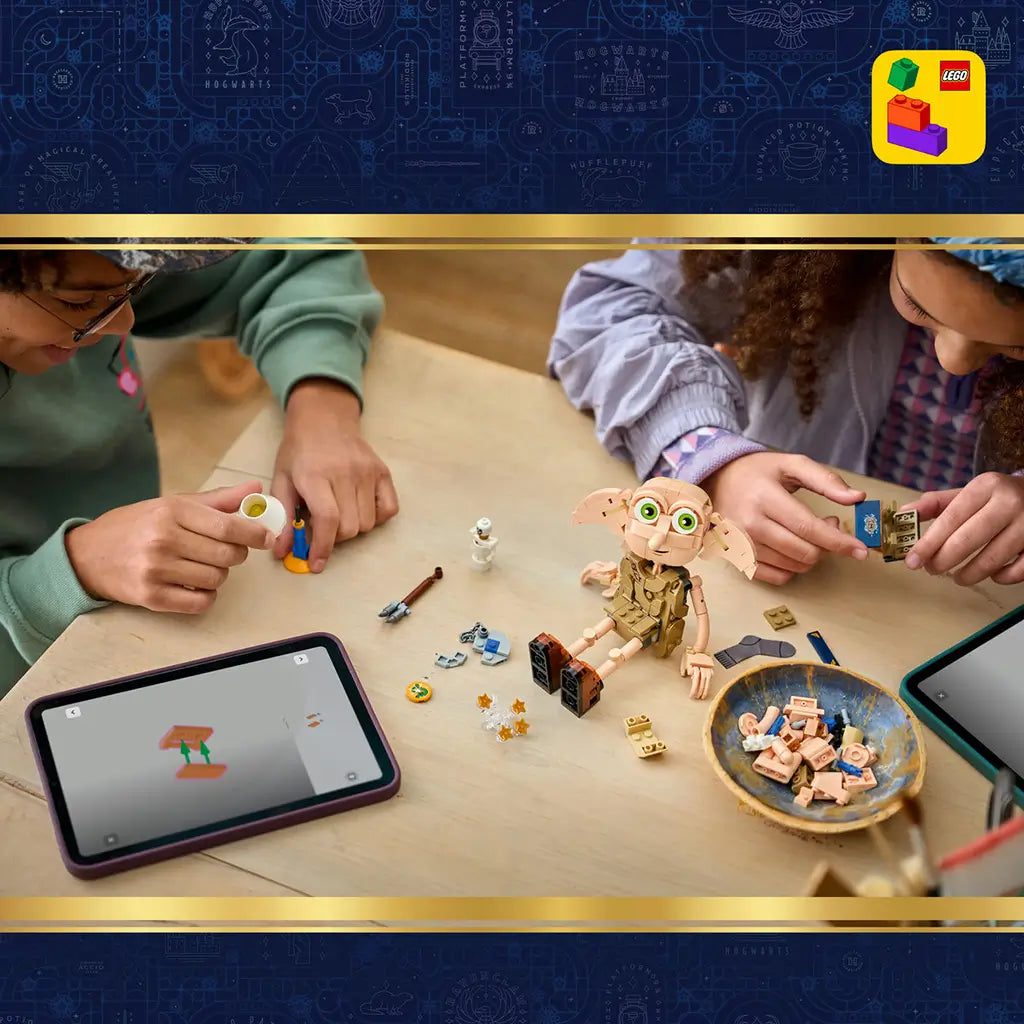 LEGO Harry Potter Dobby the Free Elf build in tan plastic bricks sits on a table as two children assemble accessories with tablets, loose pieces, a lamp and skeleton nearby.