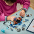 LEGO Harry Potter Forbidden Forest building scene shows a child in a pink top attaching a brown tree trunk amid blue branches, minifigures, loose bricks, and a tablet.