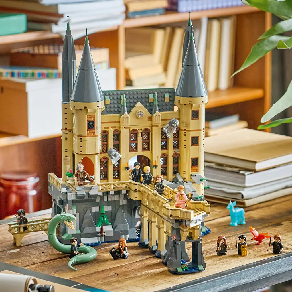 LEGO Harry Potter Hogwarts Castle East Wing display features tan walls, dark gray spires and bridge, green basilisk, minifigures, red phoenix, and blue Patronus on a wooden table.