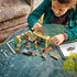 LEGO Harry Potter Herbology Class playset shows a child building the tan greenhouse with magical plants, minifigures and accessories beside a tablet on an indoor table with detailed LEGO elements and realistic display presentation.