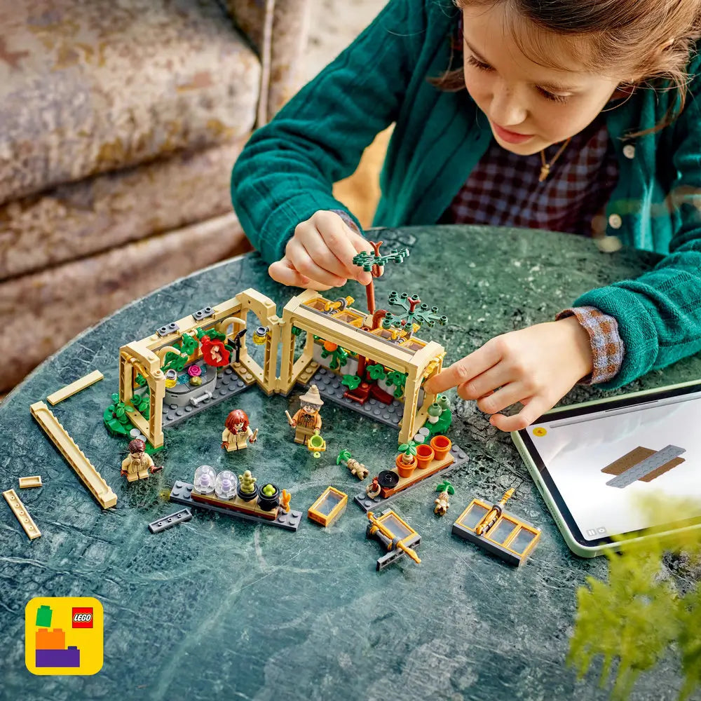 LEGO Harry Potter Herbology Class playset shows a child assembling the tan greenhouse with green plants, minifigures and digital building instructions on a tabletop indoors with detailed LEGO elements and realistic display presentation.