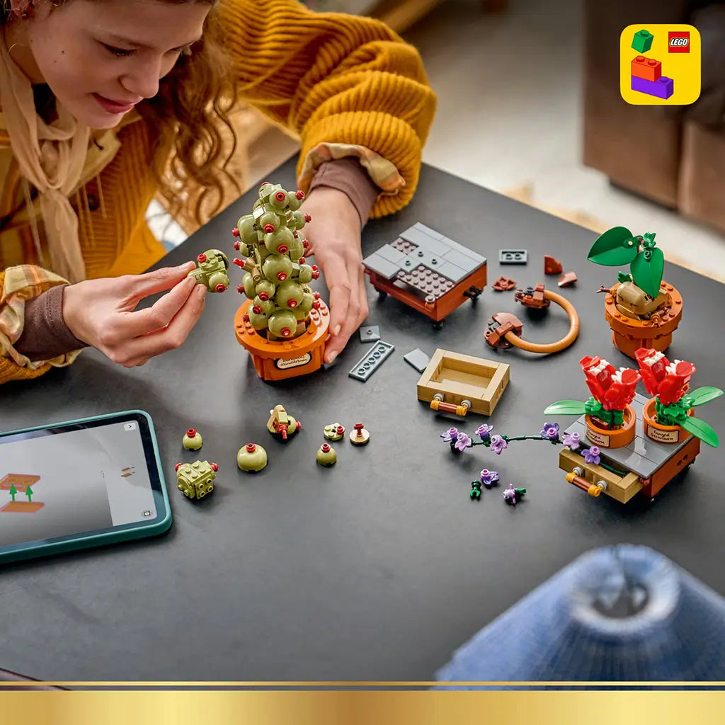 LEGO Harry Potter Hogwarts Herbology Plants building scene shows a child adding green pieces to Mimbulus Mimbletonia, with a Mandrake, red flowers, loose bricks, and a tablet.
