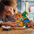 LEGO Harry Potter Hogwarts House Crest in colorful plastic bricks, held by a builder at a wooden table, with lion, snake, badger and eagle panels surrounding a central H.