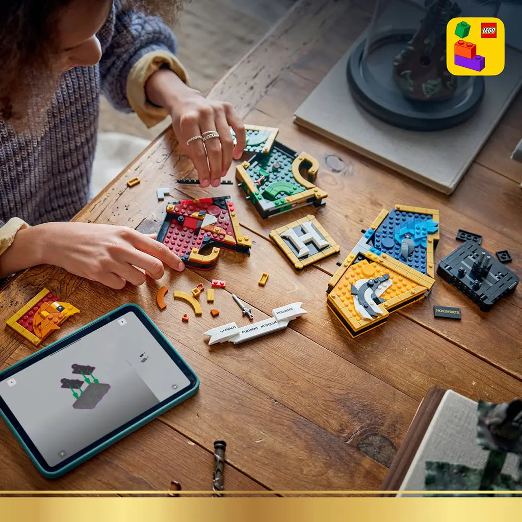 LEGO Harry Potter Hogwarts House Crest build in red, green, yellow and blue plastic bricks, shown in separate sections on a wooden table beside a tablet with digital instructions.