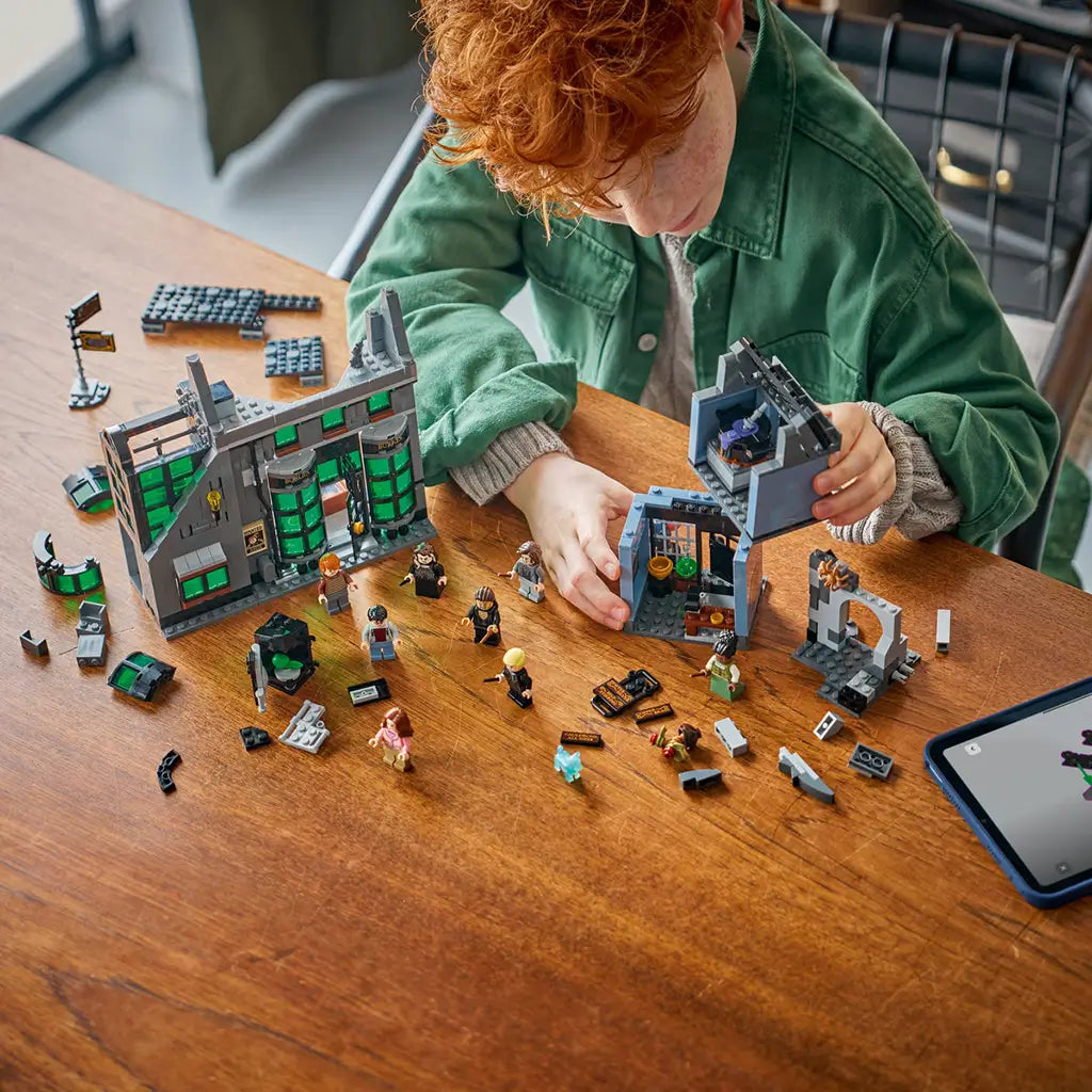 LEGO Harry Potter Knockturn Alley set in gray, black and green plastic bricks, with modular shops, minifigures and loose pieces as a child builds at a wooden table.
