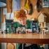 LEGO Harry Potter Knockturn Alley set in gray, black and green plastic bricks, arranged as modular shops and minifigures while a red-haired child plays at a wooden table.