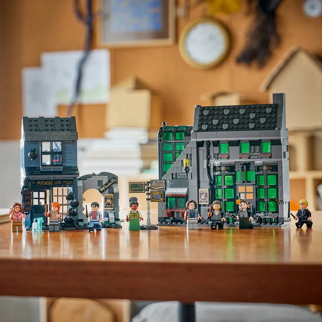 LEGO Harry Potter Knockturn Alley shops in gray, black and green plastic bricks, displayed with minifigures and street signs across a wooden table in a home setting.