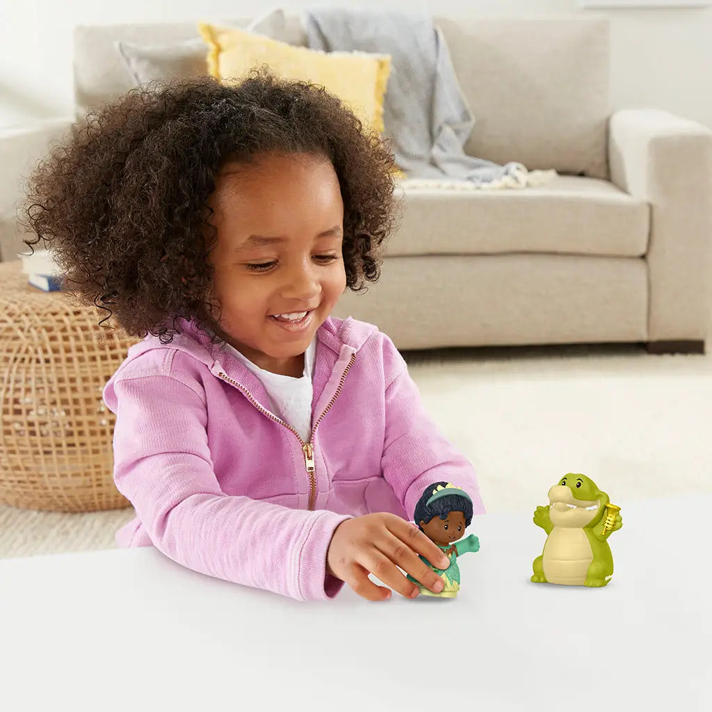 Disney Princess Tiana and Louis Little People toy figures with colorful plastic finish, smooth rounded shapes, child playing with princess and crocodile toys on table in cozy living room setting.
