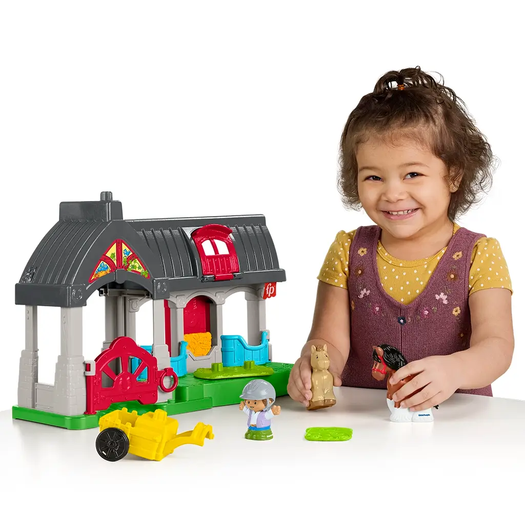 Smiling toddler playing with Fisher-Price Little People Friendly Horses Stable, interacting with horse and rider figures.