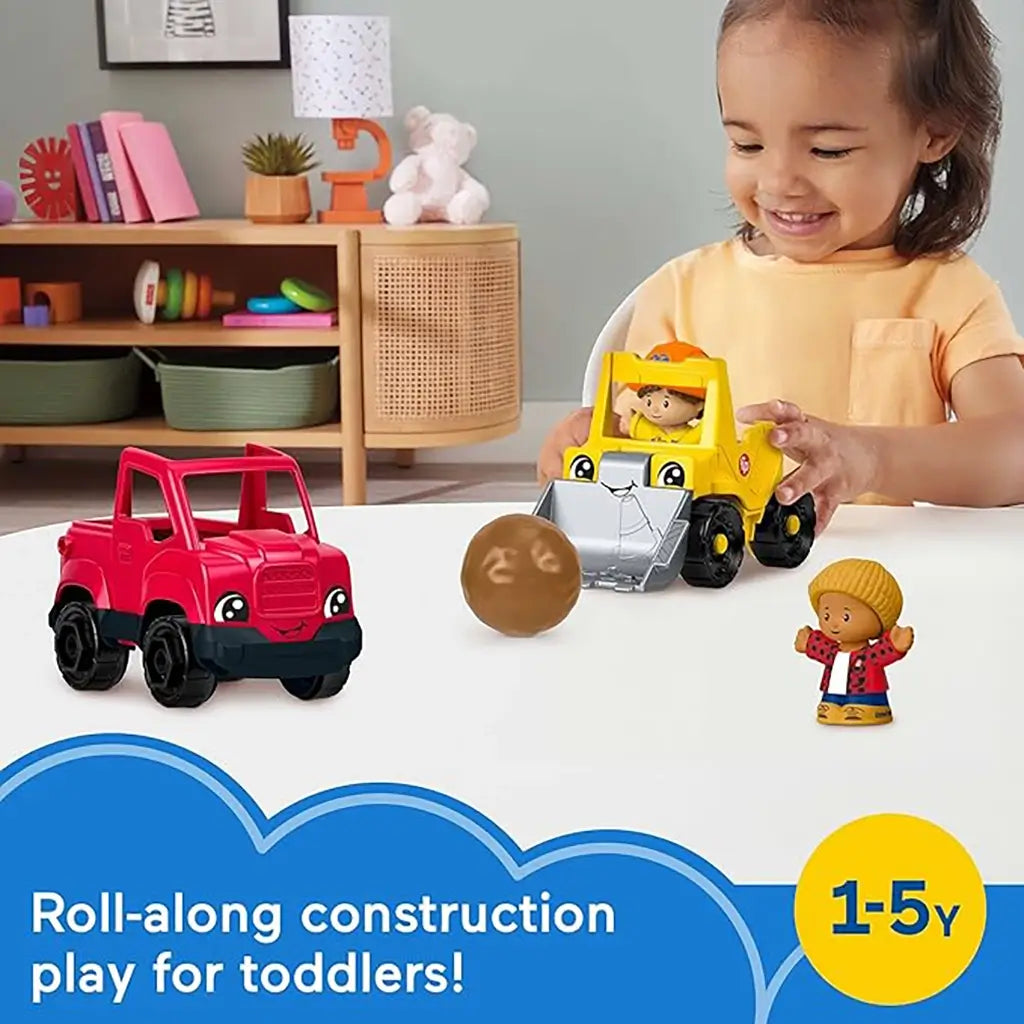Smiling toddler playing with Fisher-Price Little People Work Around Town Vehicle Set, featuring red truck, yellow loader, brown ball, and two mini worker figures on a white table.