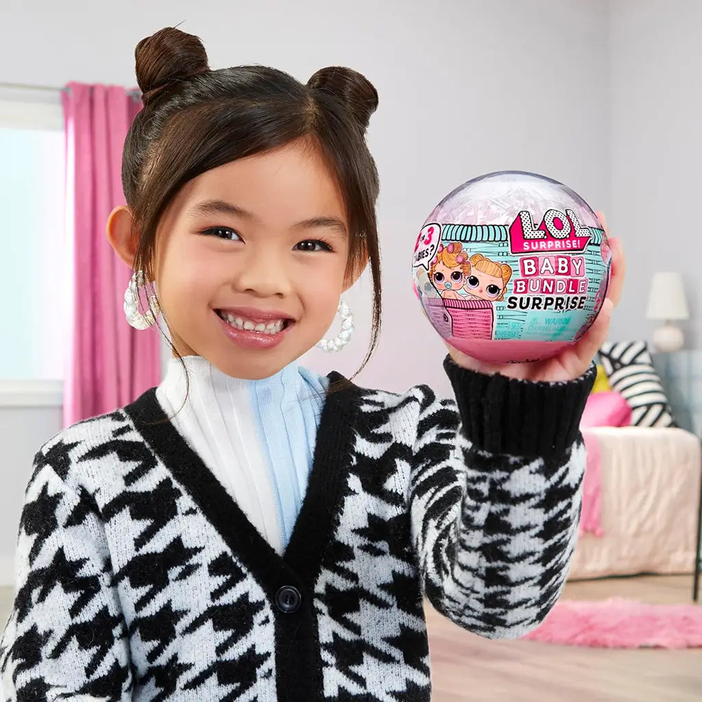 Smiling child holding an L.O.L. Surprise! Baby Bundle Surprise ball in a cozy bedroom setting, showing excitement for the collectible doll unboxing experience.