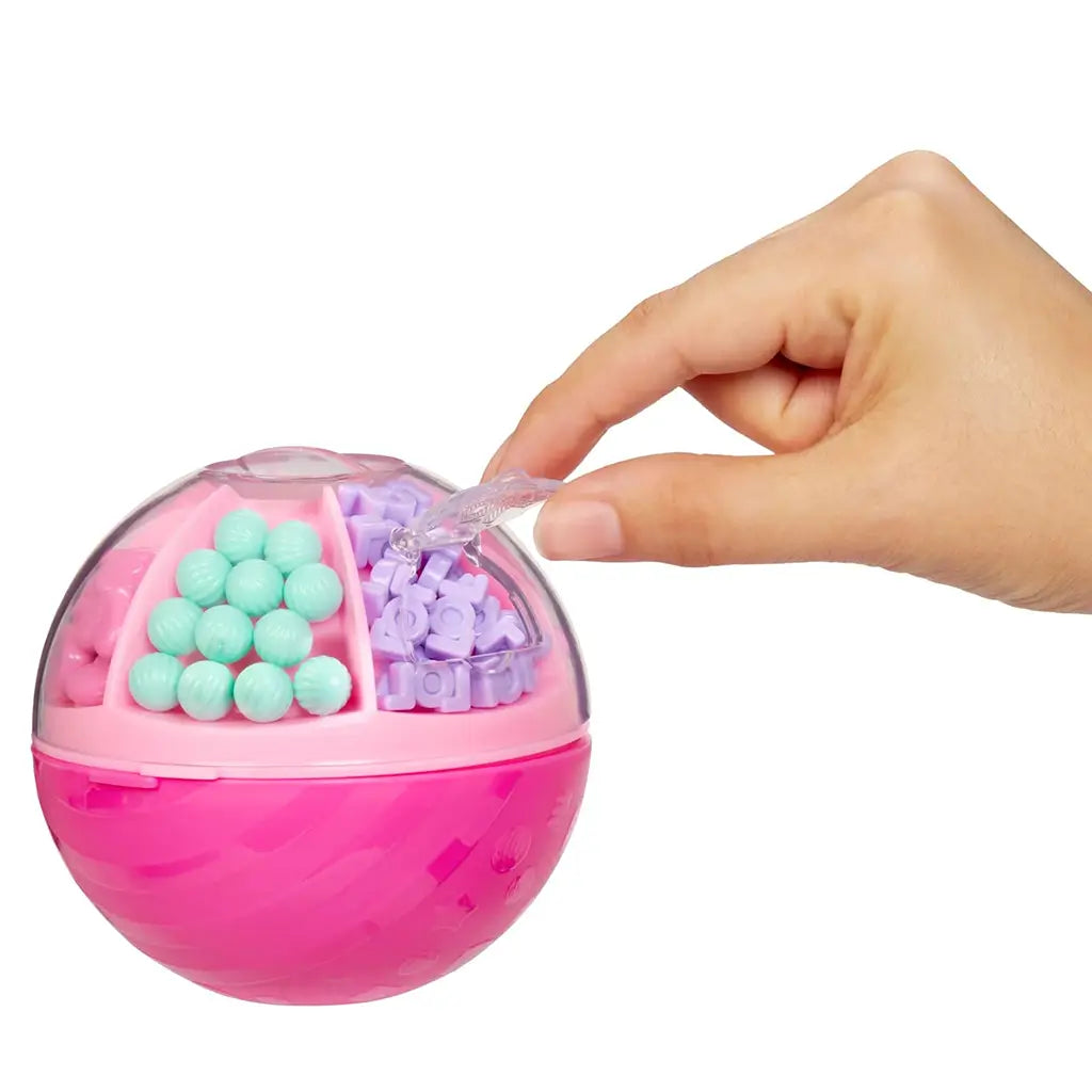 Hand opening pink LOL Surprise Hair Beads dispenser ball with compartments filled with pastel purple and mint beads designed for decorating dolls’ hair.