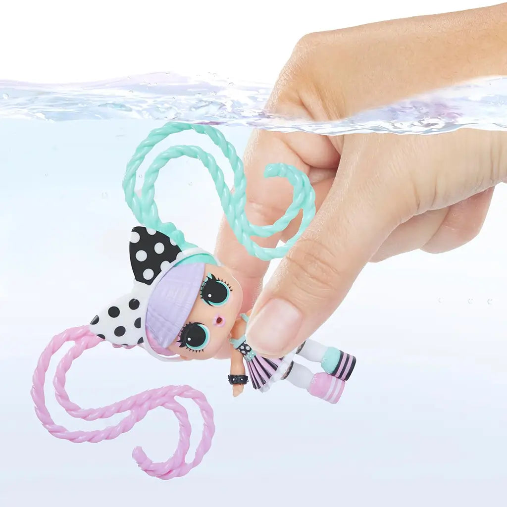 Hand dipping LOL Surprise Hair Beads doll with pastel pink and teal spiral hair into clear water, demonstrating interactive color-change or styling feature.