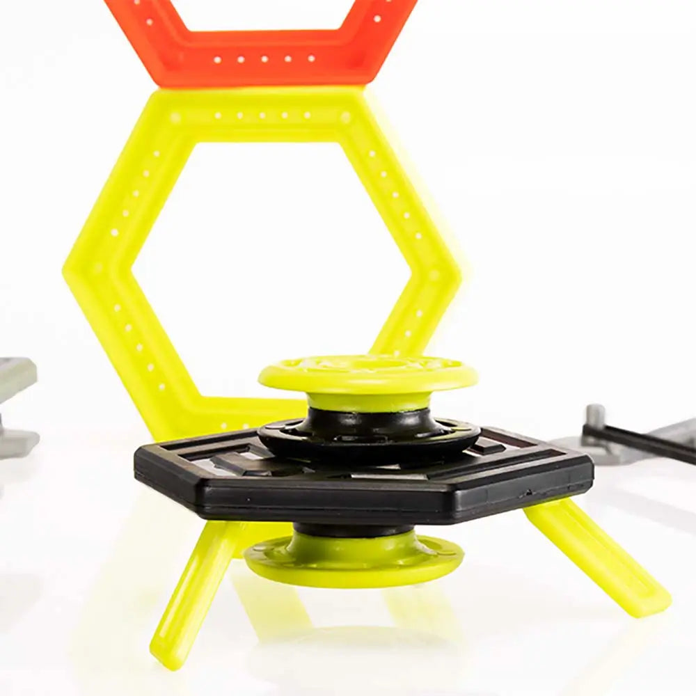 Magshuto Stunt Park magnetic launcher in black and neon yellow plastic stacked on a low hexagon platform, posed in front of tall yellow and red hexagon ring targets on a glossy white tabletop surface.