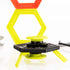 Magshuto Stunt Park magnetic launcher in black and neon yellow plastic stacked on a low hexagon platform, posed in front of tall yellow and red hexagon ring targets on a glossy white tabletop surface.