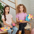Two smiling kids sitting indoors holding colorful pickleball paddles and balls from the 3C4G Adventure Fun set, featuring bright “Feel Good” and “Peace of Mind” paddle designs.