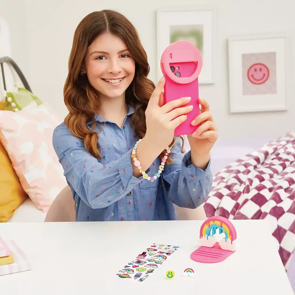 Smiling girl in a cozy bedroom holding the pink selfie light from the 3C4G Tech Accessories Set, surrounded by rainbow stickers and colorful charms on her desk.