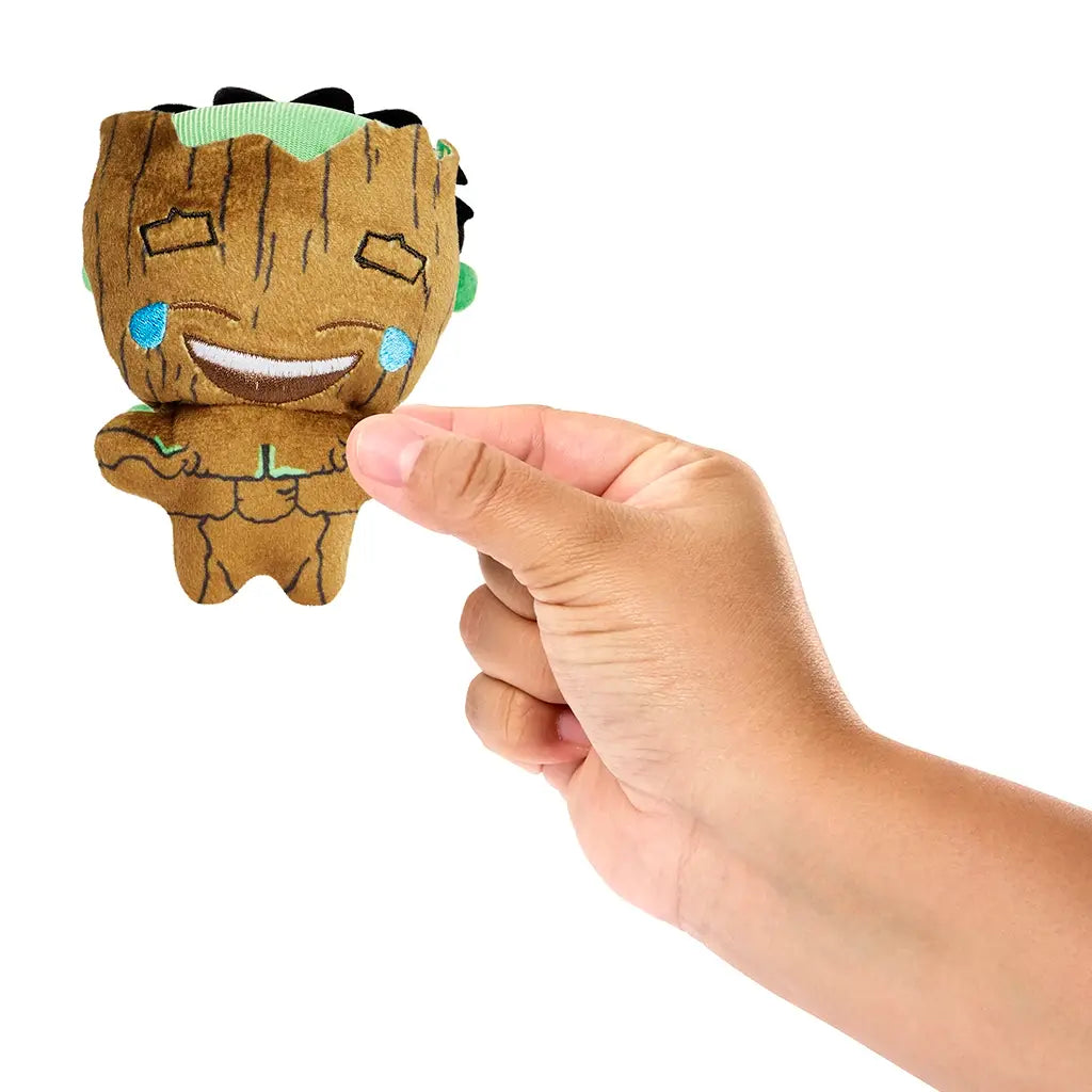 Hand holding Marvel Moodiverse Series 1 Laughing Groot plush, small soft brown figure with stitched smiling face, blue embroidered tears, and green crown detail for scale.