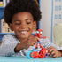 A smiling child plays with the Marvel Spidey motorcycle toy, holding the red-and-blue figure atop the matching bike with light blue wheels on a tabletop in a colorful indoor playroom setting.