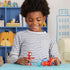 A cheerful child displays the Marvel Spidey figure and red-and-blue motorcycle with light blue wheels on a table in a bright playroom decorated with shelves and toys encouraging imaginative play.