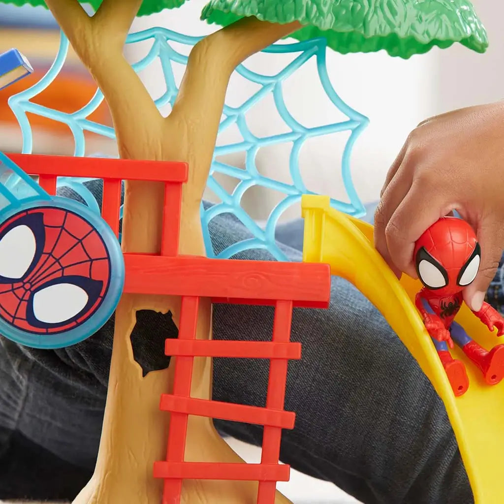 Marvel Spidey playground playset close-up captures child sliding small Spidey figure down bright yellow curved slide beside brown tree trunk and blue web lattice for active preschool role-play fun.