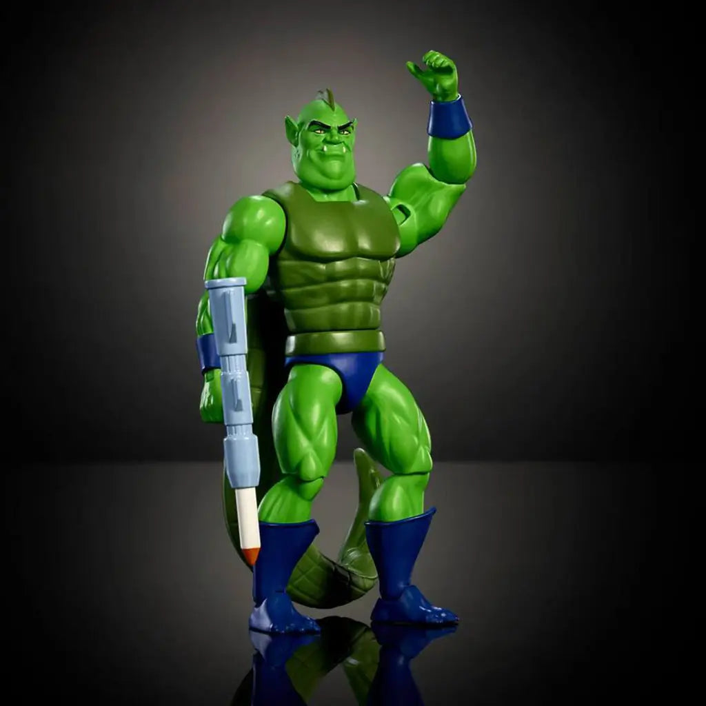 Poseable Whiplash action figure from Masters of the Universe Origins, featuring green plastic body, long segmented tail, blue armor accents, articulated limbs, and raised arm pose on a dark reflective studio surface.
