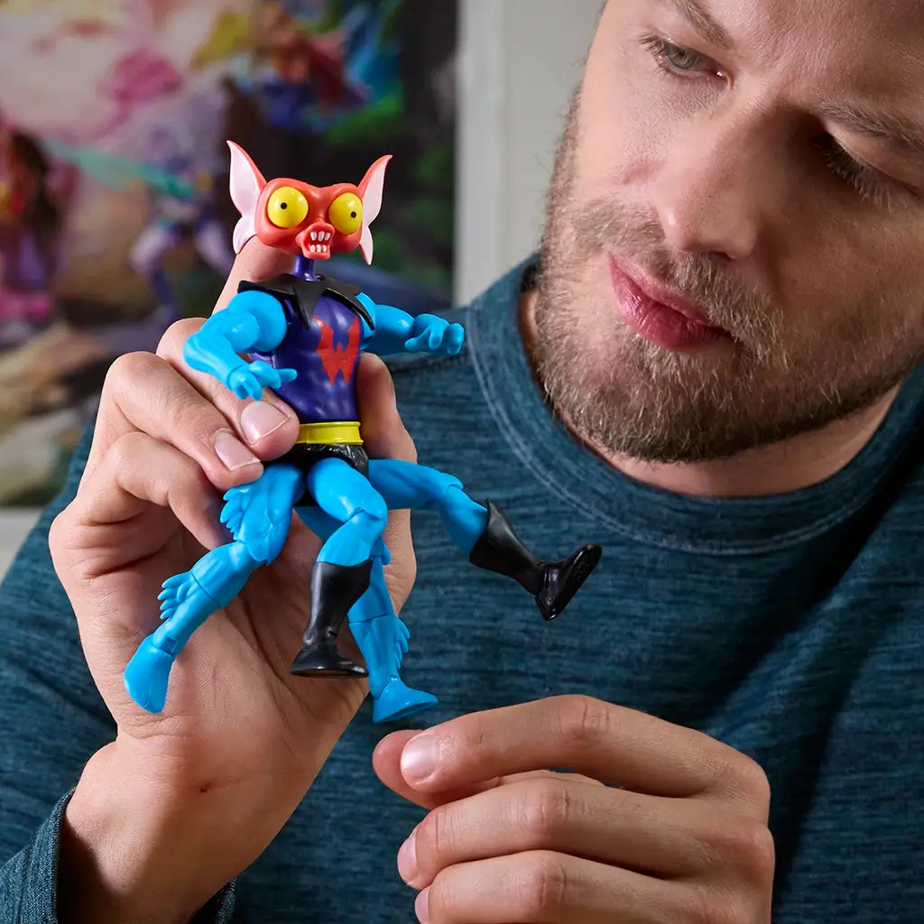 Person holding Masters of the Universe Mantenna action figure, showing red bug-like head, bright yellow eyes, and articulated blue limbs in close-up indoor setting.