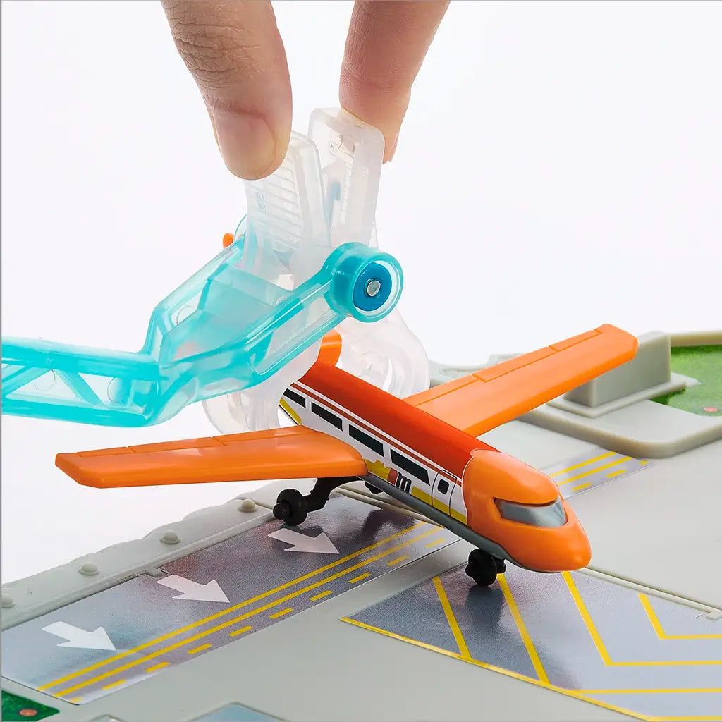 Close-up of Matchbox Airport Takeoff Adventure playset showing a transparent blue clip mechanism holding an orange toy airplane securely on the gray runway.