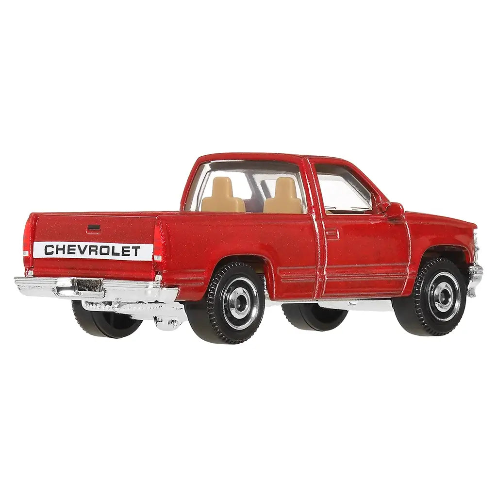 Rear angled view of red Matchbox 1995 Chevy C1500 diecast pickup with black tires, chrome bumper, tan seats, and bold CHEVROLET lettering across the tailgate.