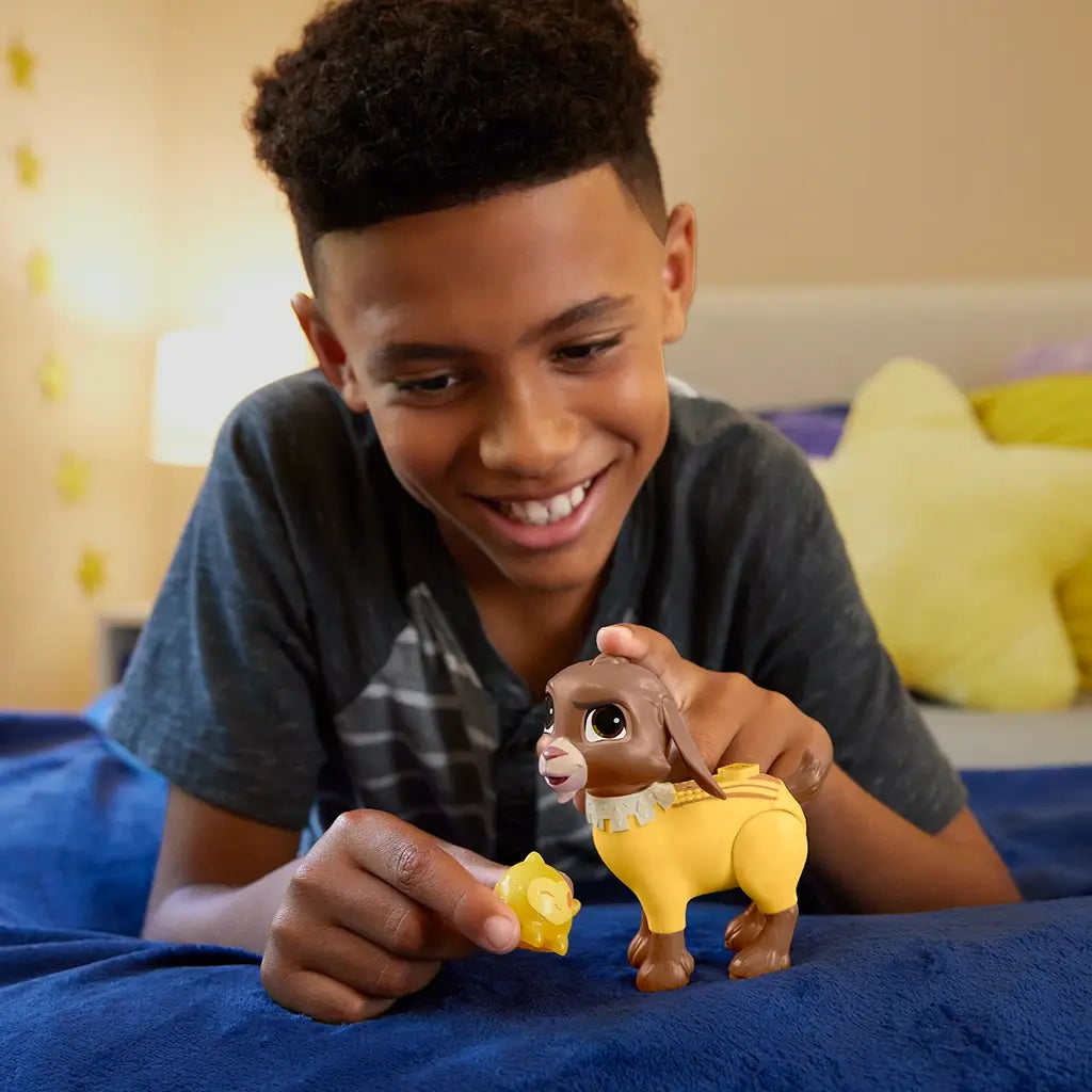 Smiling child plays with Disney Wish Valentino goat toy and glittery yellow Star accessory on a bed, demonstrating button-activated sound feature.