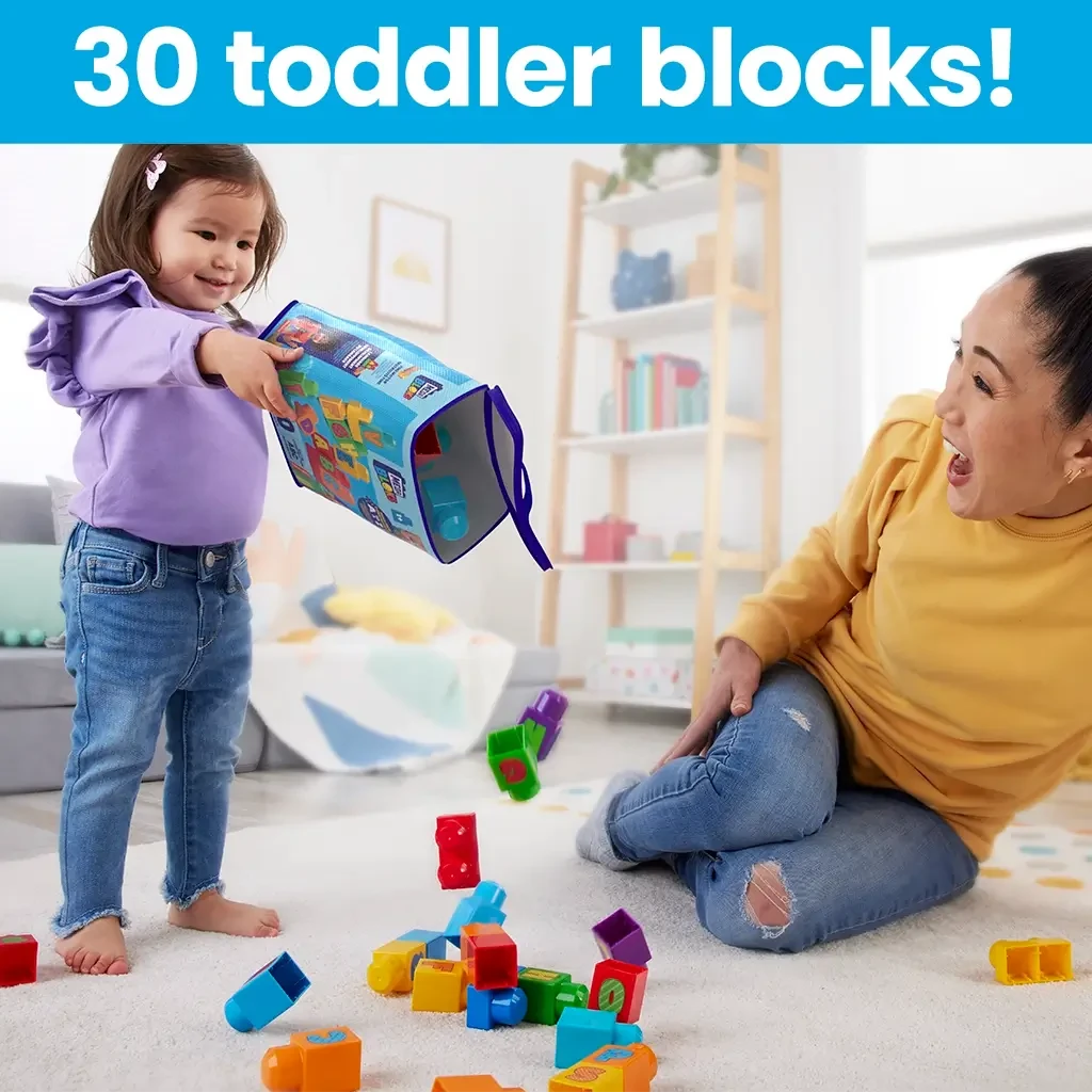 Toddler joyfully pours Mega Bloks with letters out of storage bag onto the floor while adult smiles, emphasizing interactive and educational block play.