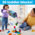 Toddler joyfully pours Mega Bloks with letters out of storage bag onto the floor while adult smiles, emphasizing interactive and educational block play.