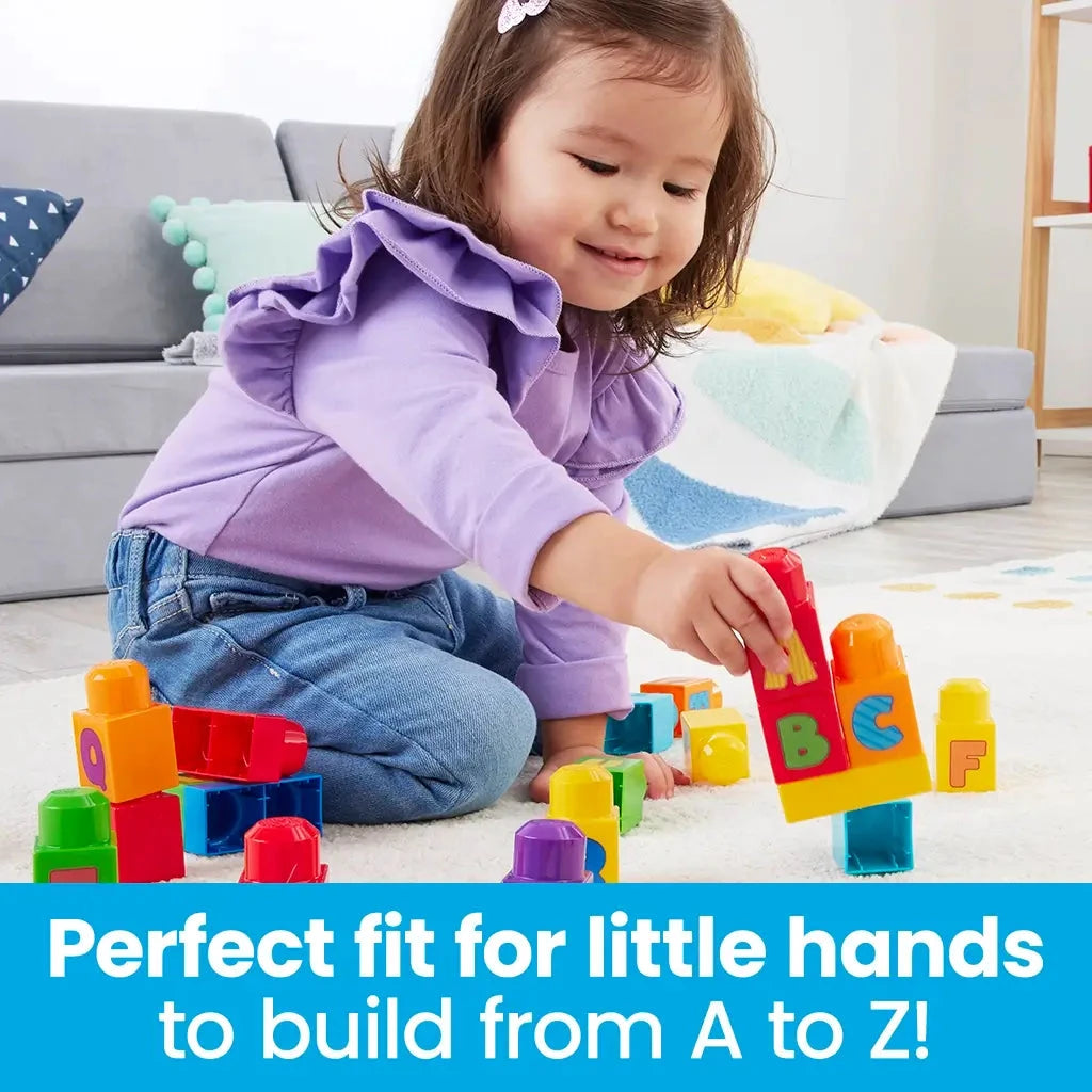Smiling toddler sits on floor placing Mega Bloks with letters onto a structure, encouraging fine motor skills and early alphabet learning through play.