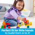 Smiling toddler sits on floor placing Mega Bloks with letters onto a structure, encouraging fine motor skills and early alphabet learning through play.