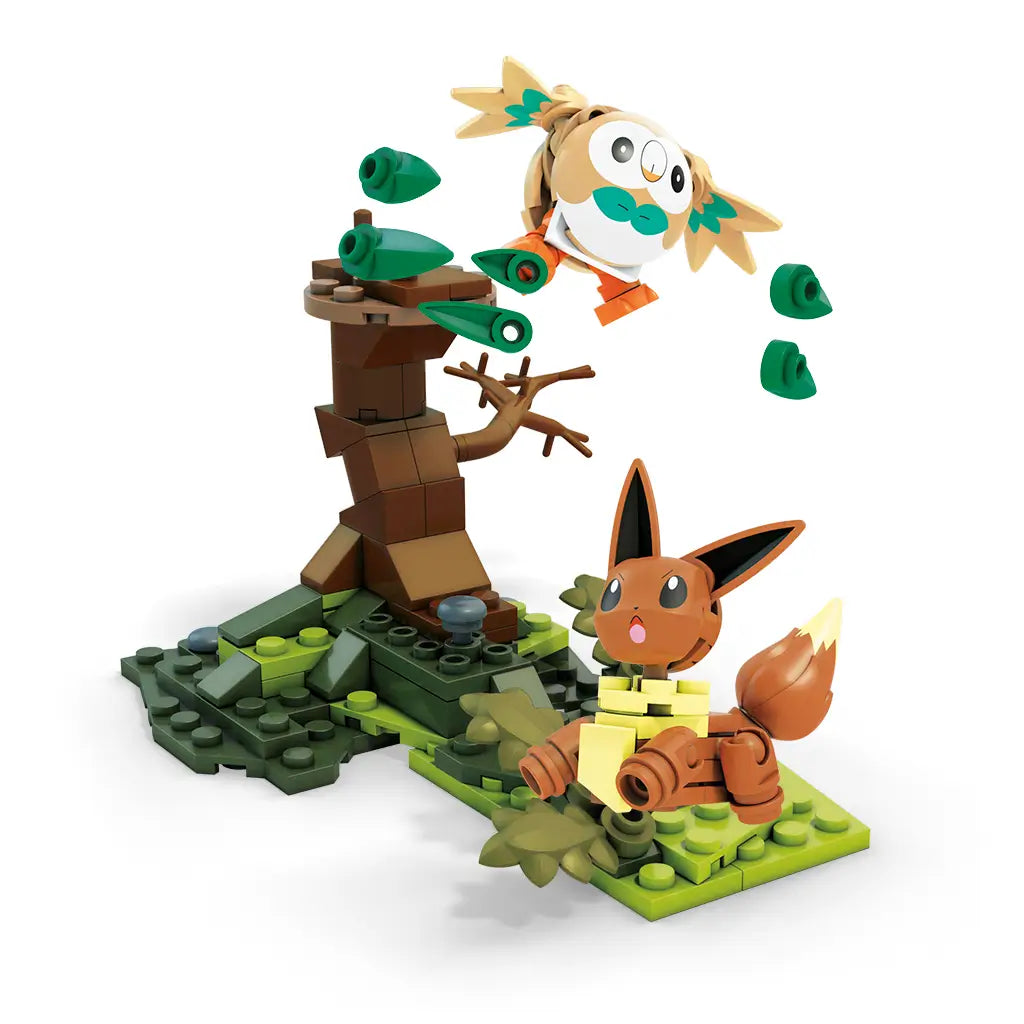 Mega Construx Pokémon building set featuring brown Rowlet with green wings flying above a blocky tree while Eevee sits on grassy terrain with leaves and stones.