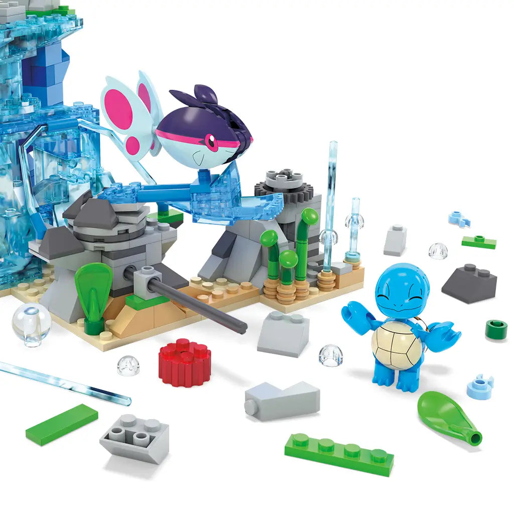Close-up of Mega Pokémon Aquatic Adventure set with blue waterfall blocks, rocks, plants, Squirtle figure on ground, and Finneon mid-jump, surrounded by loose building pieces.