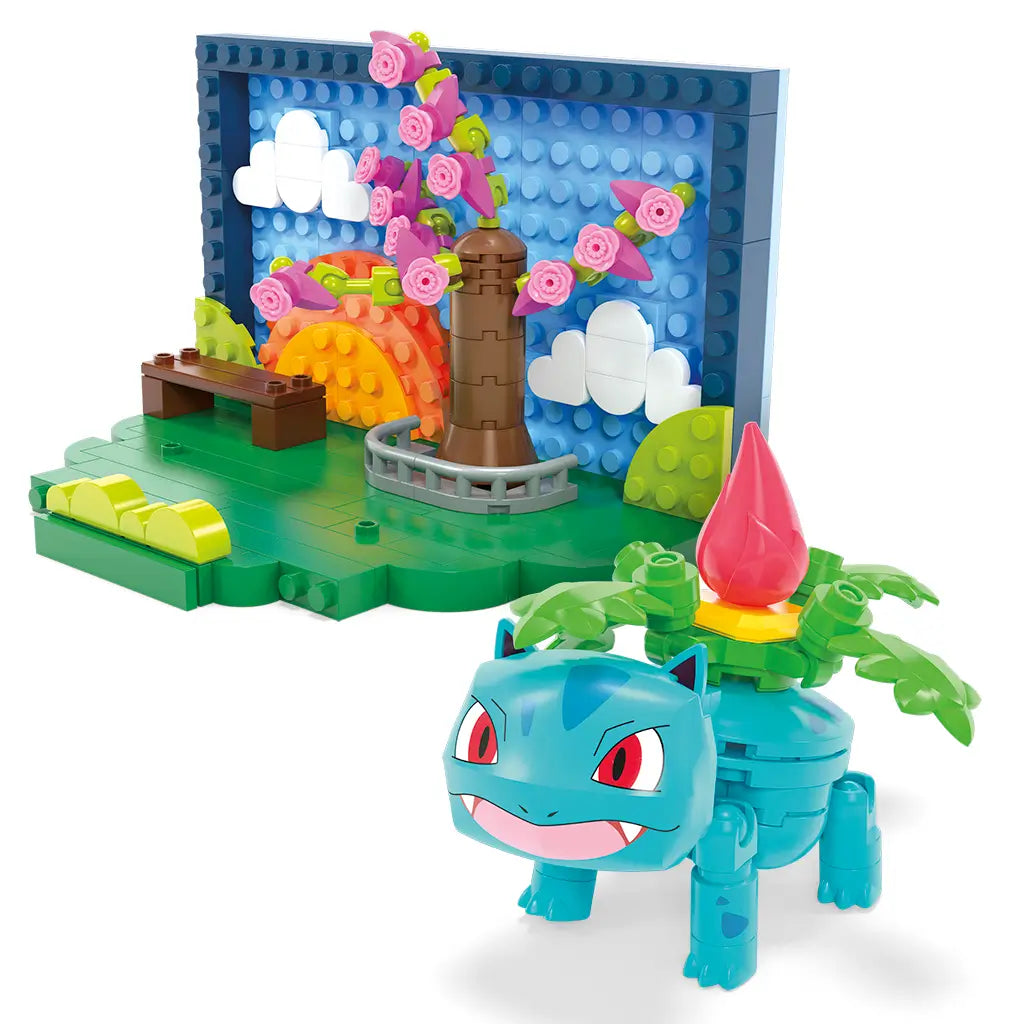 Angled view of Mega Pokémon Park Scene set shows Ivysaur figure in front of park diorama with tree of pink flowers, bench, and blocky orange sunset background against blue sky.
