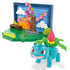 Angled view of Mega Pokémon Park Scene set shows Ivysaur figure in front of park diorama with tree of pink flowers, bench, and blocky orange sunset background against blue sky.