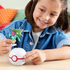 Smiling child in denim jacket holding Mega Pokémon Dreepy figure above white Poké Ball toy on wooden table in bright indoor playroom setting. This Mega Construx building set includes 21 pieces for creative play, recommended for Pokémon fans ages six and older.