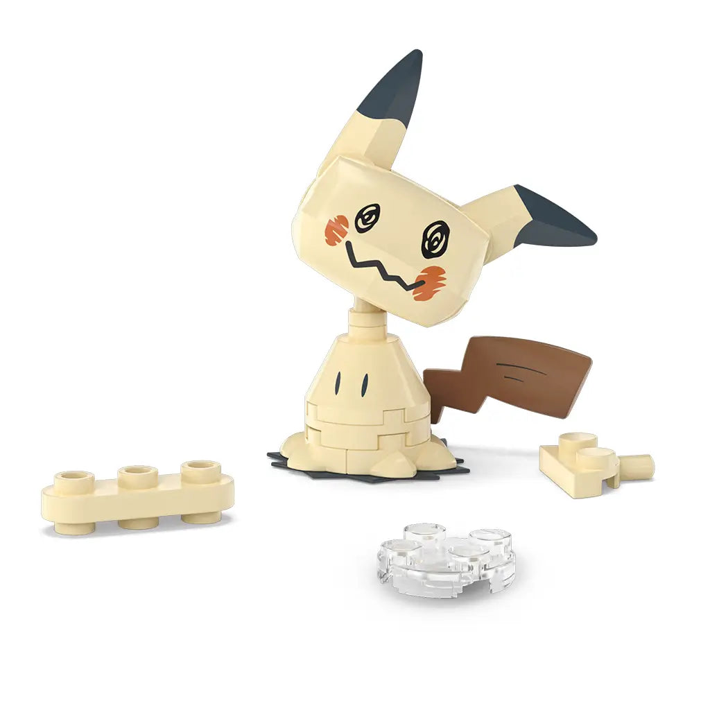 Unassembled Mega Pokémon Mimikyu building set pieces laid out, including beige body parts, brown tail, and small clear base elements. This collector-friendly Mega Construx toy is ideal for fans ages